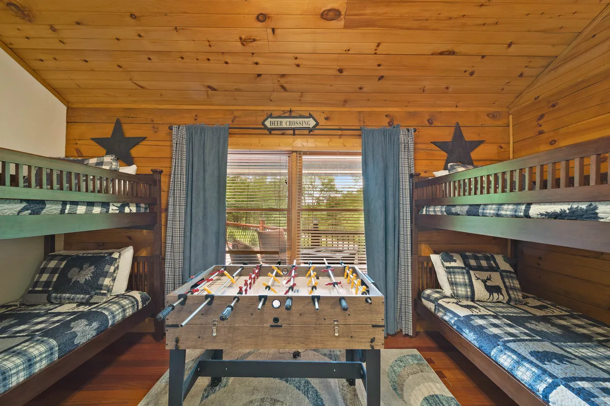 A fun, family-focused room with bunk beds, a foosball table, and large windows letting in natural light. The setup is perfect for game nights and cozy storytelling sessions, with playful vibes and views of the outdoors.