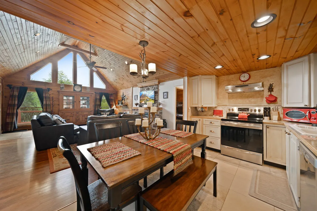 An open dining area flows seamlessly into a thoughtfully designed kitchen, all beneath rustic wooden ceilings and with large windows allowing natural light to fill the space. The setup highlights ample room for shared meals, celebrations, and relaxed gatherings.