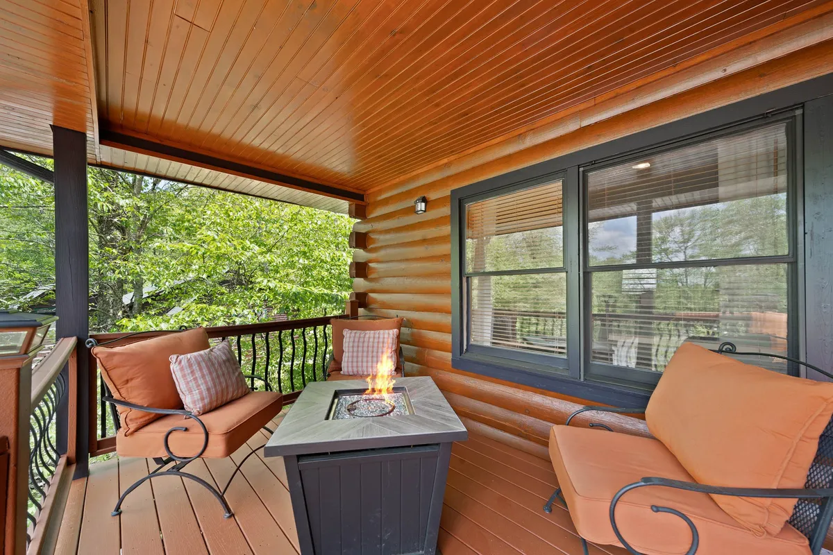 This exterior shot features a fire pit surrounded by comfortable seating and wooden logs, set against a backdrop of natural foliage. The scene evokes warmth and gathering, even in cooler weather.