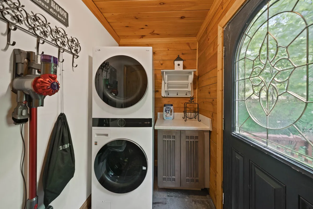 A practical yet cozy utility area with a stacked washer and dryer, decorative wall hooks, wooden cabinetry, and a glass door. The space feels both functional and welcoming—ideal for managing laundry and stowing gear between outdoor excursions, ensuring guests' comfort throughout every season.